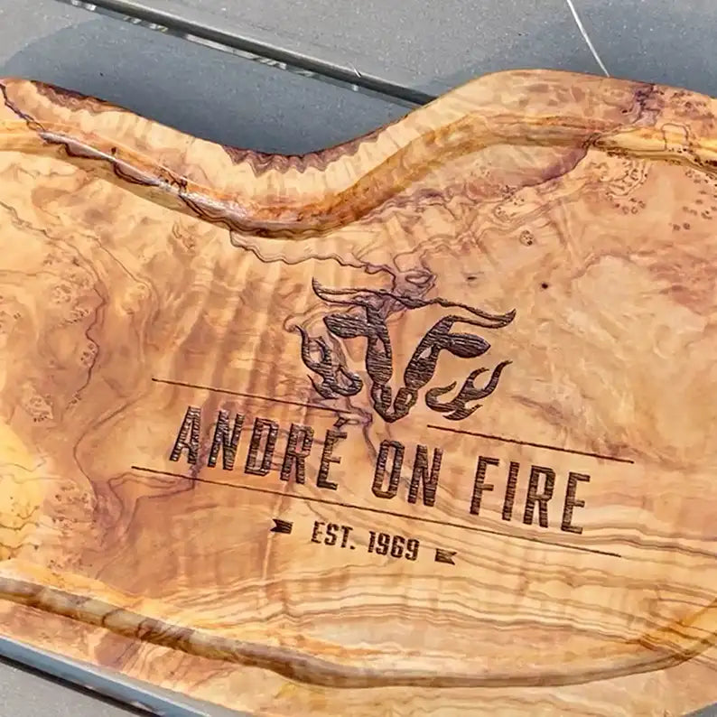 Motiv "On Fire" mit stilisiertem Rinderkopf mit Flammen und Personaliserungsoption mit Name in Großbuchstaben und Datum - Mediterranes Schneidebrett aus Olivenholz mit Saftrille mit und ohne Grifflasche oder Handgriff - Personalisiertes Männergeschenk von Jeske Design