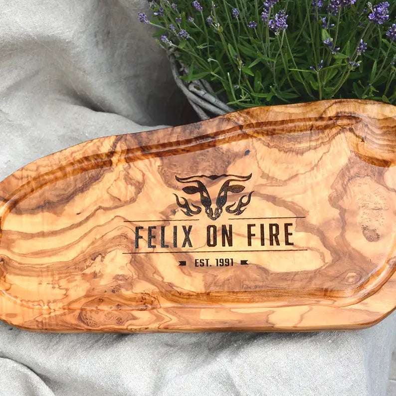 Motiv "On Fire" mit stilisiertem Rinderkopf mit Flammen und Personaliserungsoption mit Name in Großbuchstaben und Datum - Mediterranes Schneidebrett aus Olivenholz mit Saftrille mit und ohne Grifflasche oder Handgriff - Personalisiertes Männergeschenk von Jeske Design