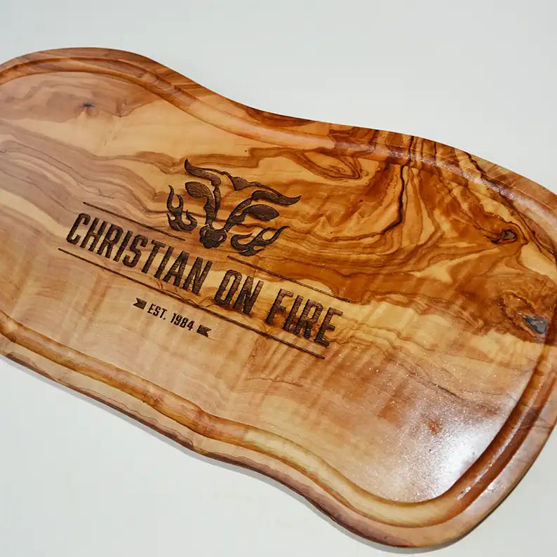 Motiv "On Fire" mit stilisiertem Rinderkopf mit Flammen und Personaliserungsoption mit Name in Großbuchstaben und Datum - Mediterranes Schneidebrett aus Olivenholz mit Saftrille mit und ohne Grifflasche oder Handgriff - Personalisiertes Männergeschenk von Jeske Design