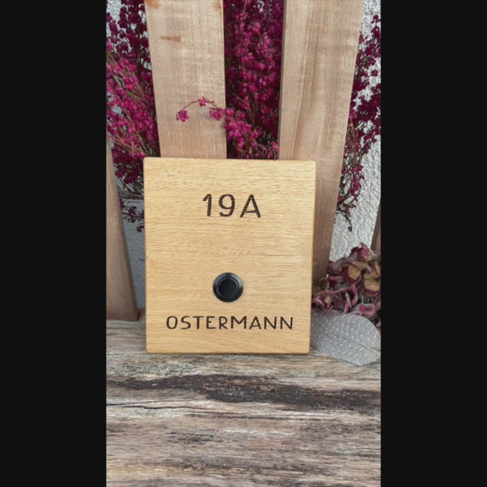 Klingelschild aus edler Eiche mit Edelstahl Taster unbeleuchtet oder mit weißem LED-Licht oder schwarz-Aluminium-Taster in der Größe 12 x 14 cm oder 14 x 25 cm. Motiv mit einer Retro Schrift wird mit dem Nachnamen - optional mit Vornamen oder “Familie” oder “Herzlich Willkommen” - per Laser in das Holz graviert. Schriftart: Retro Handschrift. Hier mit Nachname und schwarzen Aluminiumtaster.
