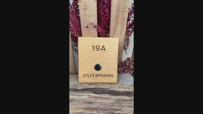 Klingelschild aus edler Eiche mit Edelstahl Taster unbeleuchtet oder mit weißem LED-Licht oder schwarz-Aluminium-Taster in der Größe 12 x 14 cm oder 14 x 25 cm. Motiv mit einer Retro Schrift wird mit dem Nachnamen - optional mit Vornamen oder “Familie” oder “Herzlich Willkommen” - per Laser in das Holz graviert. Schriftart: Retro Handschrift. Hier mit Nachname und schwarzen Aluminiumtaster.