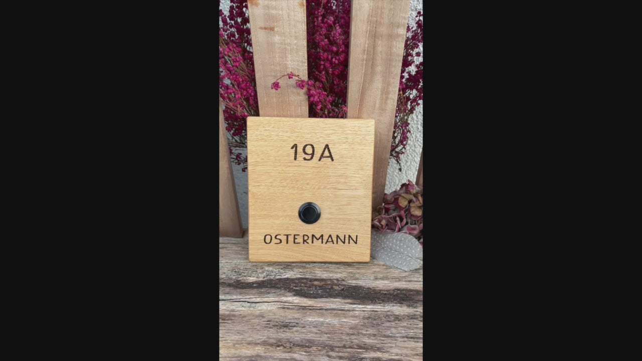Klingelschild aus edler Eiche mit Edelstahl Taster unbeleuchtet oder mit weißem LED-Licht oder schwarz-Aluminium-Taster in der Größe 12 x 14 cm oder 14 x 25 cm. Motiv mit einer Retro Schrift wird mit dem Nachnamen - optional mit Vornamen oder “Familie” oder “Herzlich Willkommen” - per Laser in das Holz graviert. Schriftart: Retro Handschrift. Hier mit Nachname und schwarzen Aluminiumtaster.