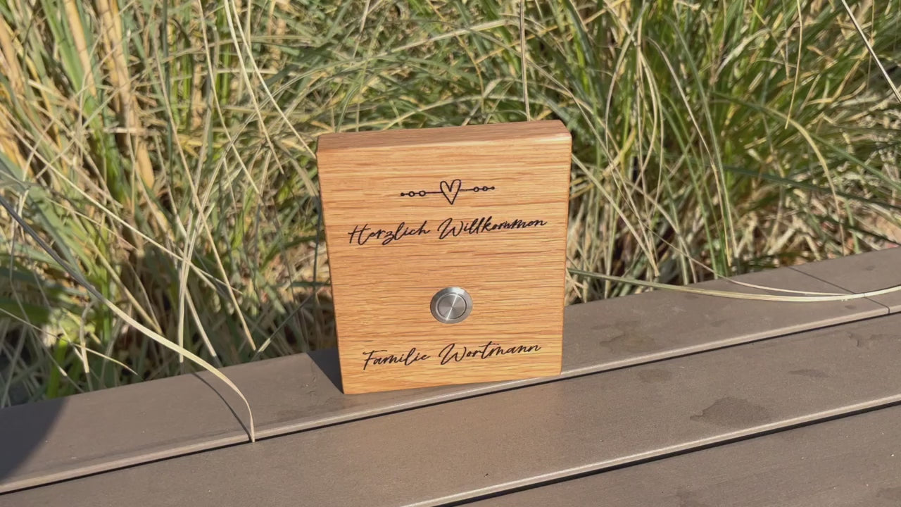 Klingelschild aus edler Eiche mit Edelstahl Taster unbeleuchtet oder mit weißem LED-Licht oder schwarzen Aluminium-Taster in der Größe 12 x 14 cm oder 14 x 25 cm. Verspieltes Motiv mit einem Herz und vier Kreisen auf einer Linie mit Herzlich Willkommen und Deinem Nachnamen - optional mit Vornamen oder “Familie” - wird per Laser in das Holz graviert. Schriftart: Geschwungene Handschrift. Hier mit Edelstahltaster matt.