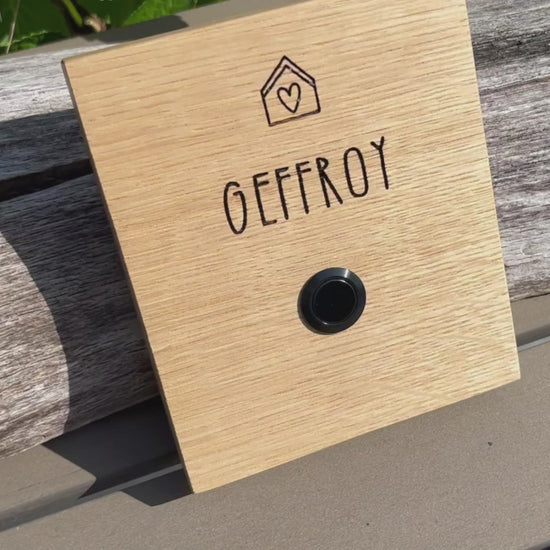 Klingelschild aus edler Eiche mit Edelstahl Taster unbeleuchtet oder mit weißem LED-Licht oder schwarz-Aluminium-Taster in der Größe 12 x 14 cm oder 14 x 25 cm. Motiv Haus & Herz wird mit dem Nachnamen - optional mit Vornamen oder “Familie” oder “Herzlich Willkommen” - per Laser in das Holz graviert. Schriftart: gradlinige Handschrift. Hier mit Nachnamen und schwarzem Aluminiumtaster. 
