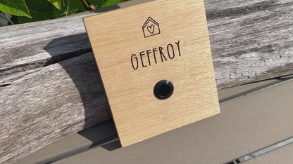 Klingelschild aus edler Eiche mit Edelstahl Taster unbeleuchtet oder mit weißem LED-Licht oder schwarz-Aluminium-Taster in der Größe 12 x 14 cm oder 14 x 25 cm. Motiv Haus & Herz wird mit dem Nachnamen - optional mit Vornamen oder “Familie” oder “Herzlich Willkommen” - per Laser in das Holz graviert. Schriftart: gradlinige Handschrift. Hier mit Nachnamen und schwarzem Aluminiumtaster. 