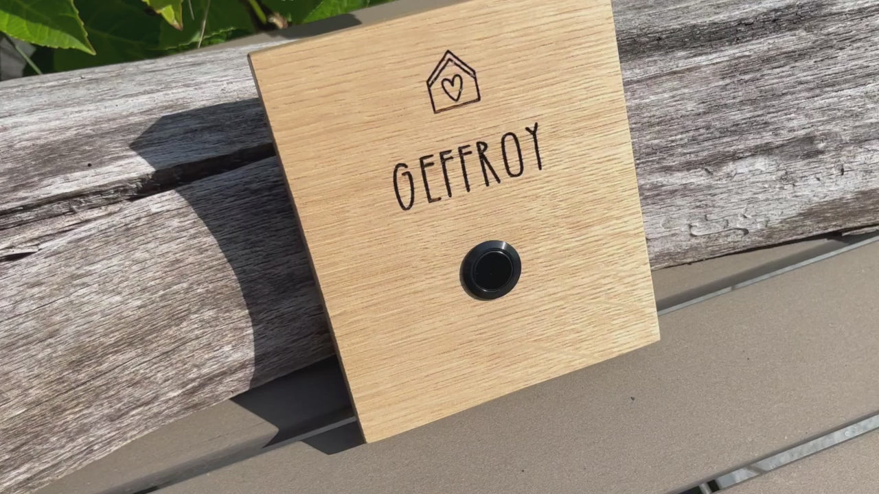 Klingelschild aus edler Eiche mit Edelstahl Taster unbeleuchtet oder mit weißem LED-Licht oder schwarz-Aluminium-Taster in der Größe 12 x 14 cm oder 14 x 25 cm. Motiv Haus & Herz wird mit dem Nachnamen - optional mit Vornamen oder “Familie” oder “Herzlich Willkommen” - per Laser in das Holz graviert. Schriftart: gradlinige Handschrift. Hier mit Nachnamen und schwarzem Aluminiumtaster. 